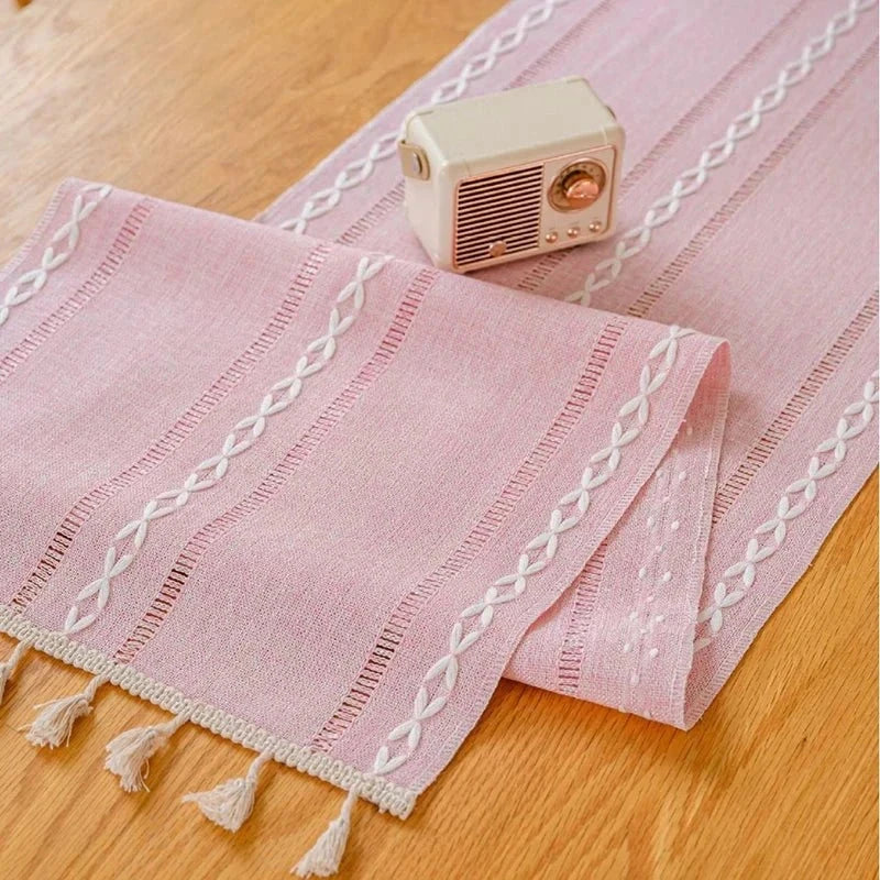 Woven natural cotton table runner with macrame embroidery and tassels on a wooden dining table.