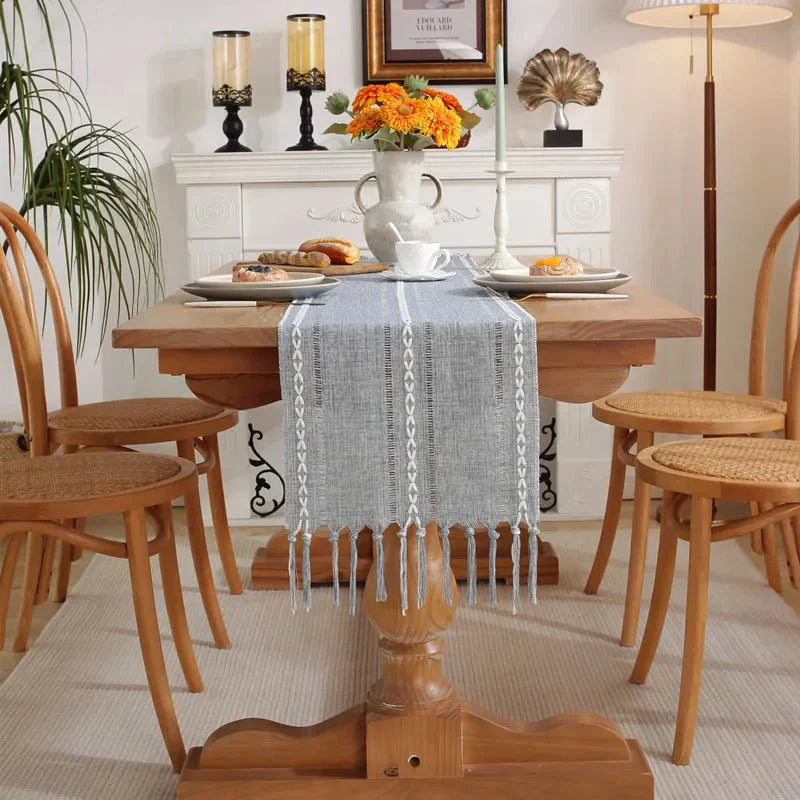 Woven natural cotton table runner with rustic design and macrame embroidery on wooden dining table.