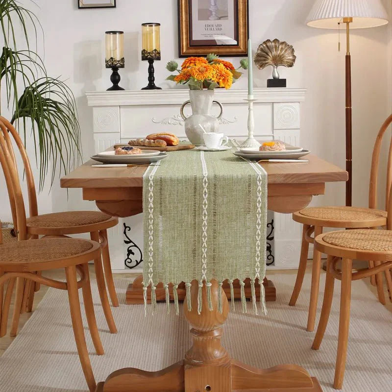 Woven natural cotton table runner with rustic farmhouse design, featuring macrame embroidery and tassels on a wooden dining table.