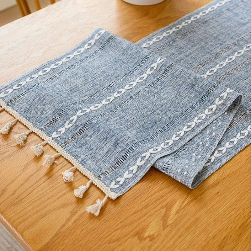 Woven cotton table runner with tassels and macrame embroidery on a wooden dining table.