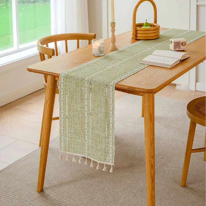 Woven natural cotton table runner on wooden dining table with rustic macrame embroidery.