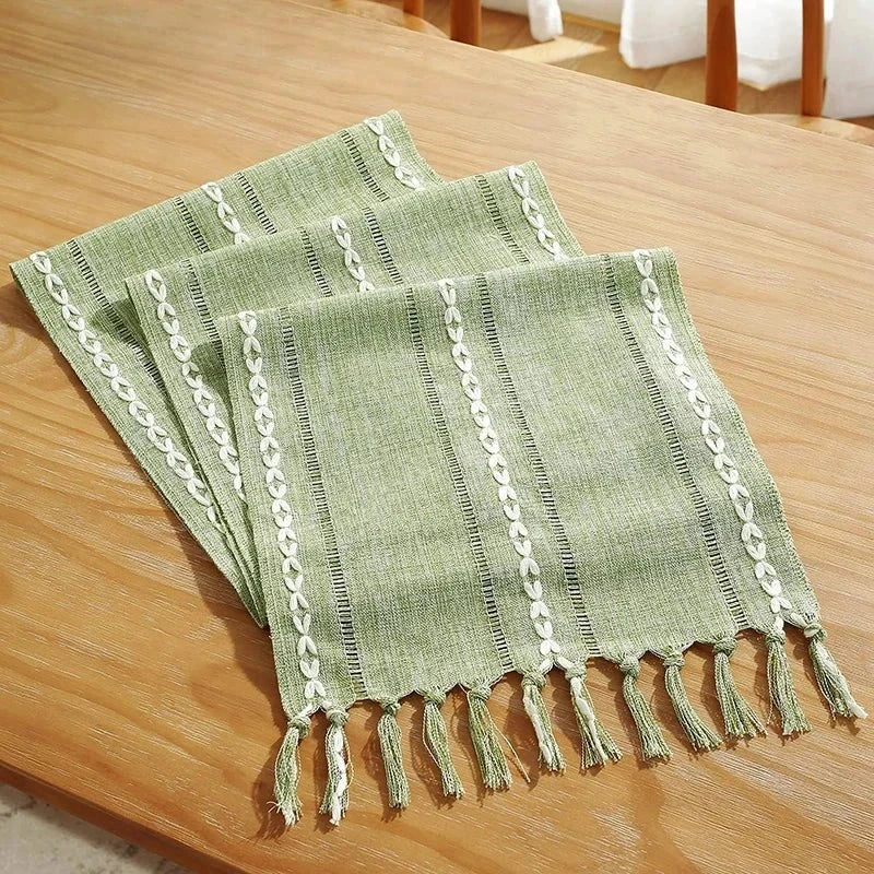 Woven natural cotton table runner with macrame details on a wooden dining table.