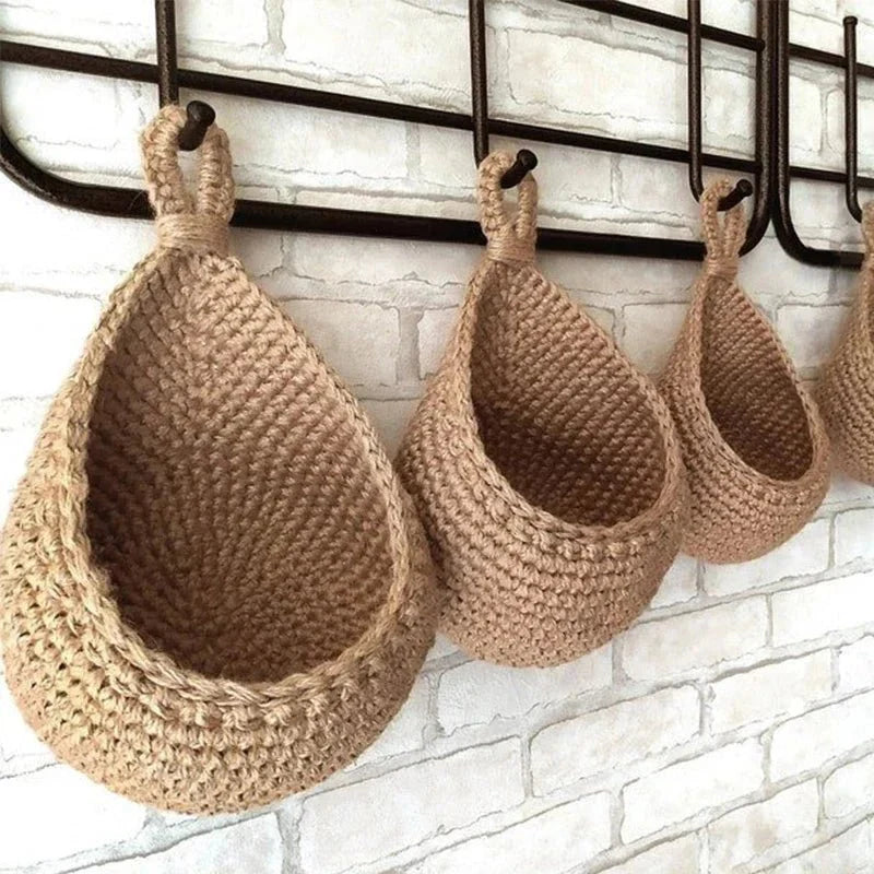Woven teardrop-shaped wall basket hanging from a rail, made of natural fiber rope with an organic crocheted texture.