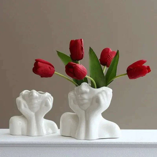 Ceramic sculptural vase with face design holding vibrant red tulips, decorative centerpiece.