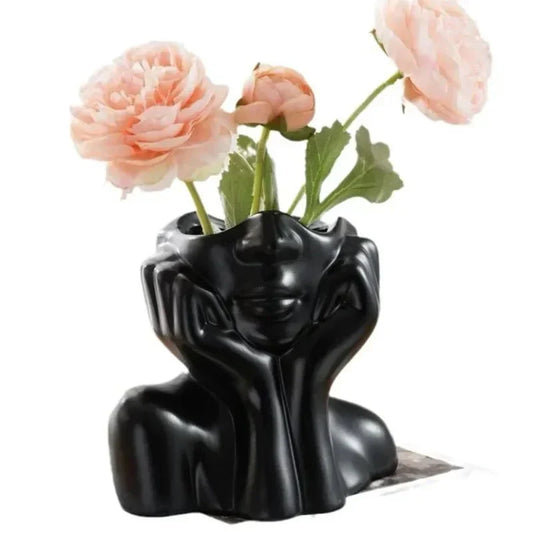 Sculptural black ceramic vase with floral decoration, shaped like a resting face.