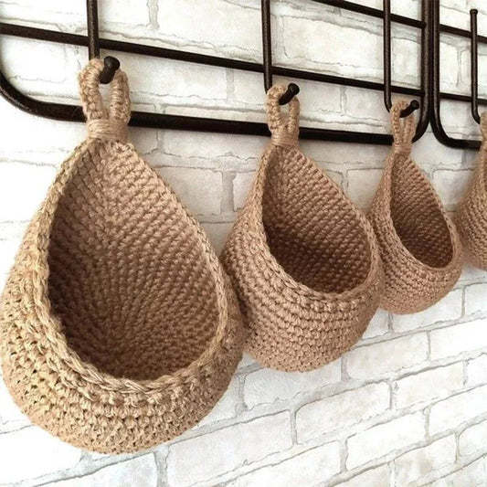 Woven teardrop-shaped wall basket hanging from a rail, made of natural fiber rope with an organic crocheted texture.