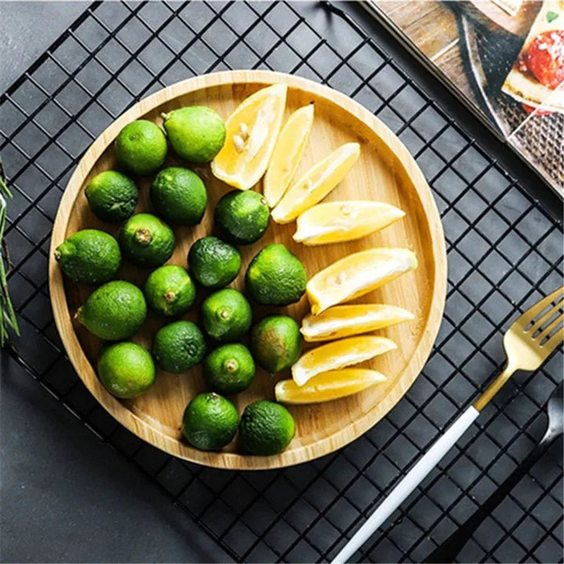 Round wooden serving tray with green limes and lemon wedges.