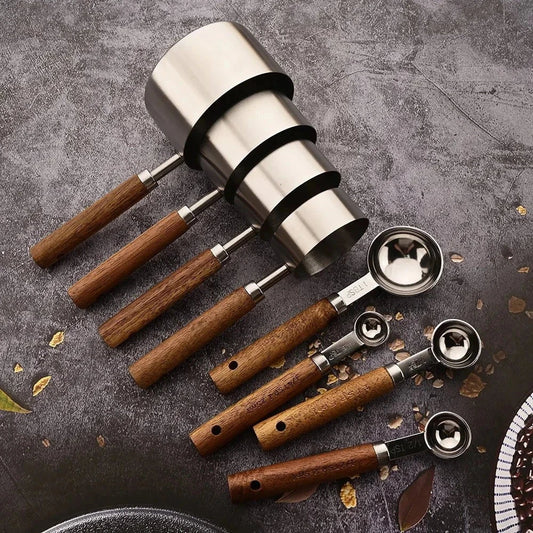 Stainless steel measuring spoons set with wooden handles on a dark surface.